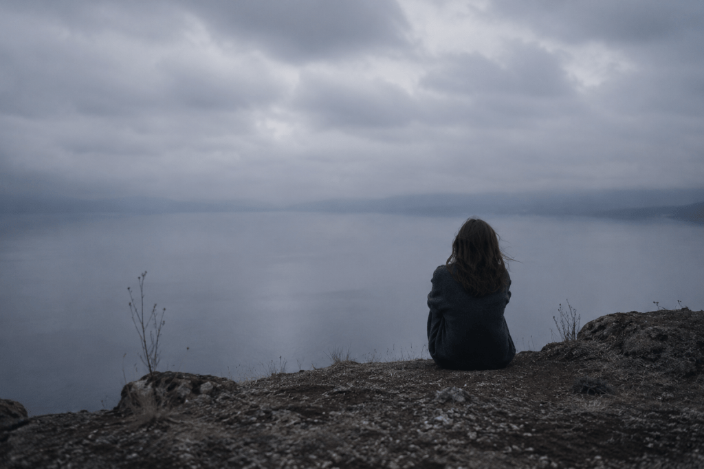 Una mujer joven, de espaldas, contemplando un lago, al atardecer
